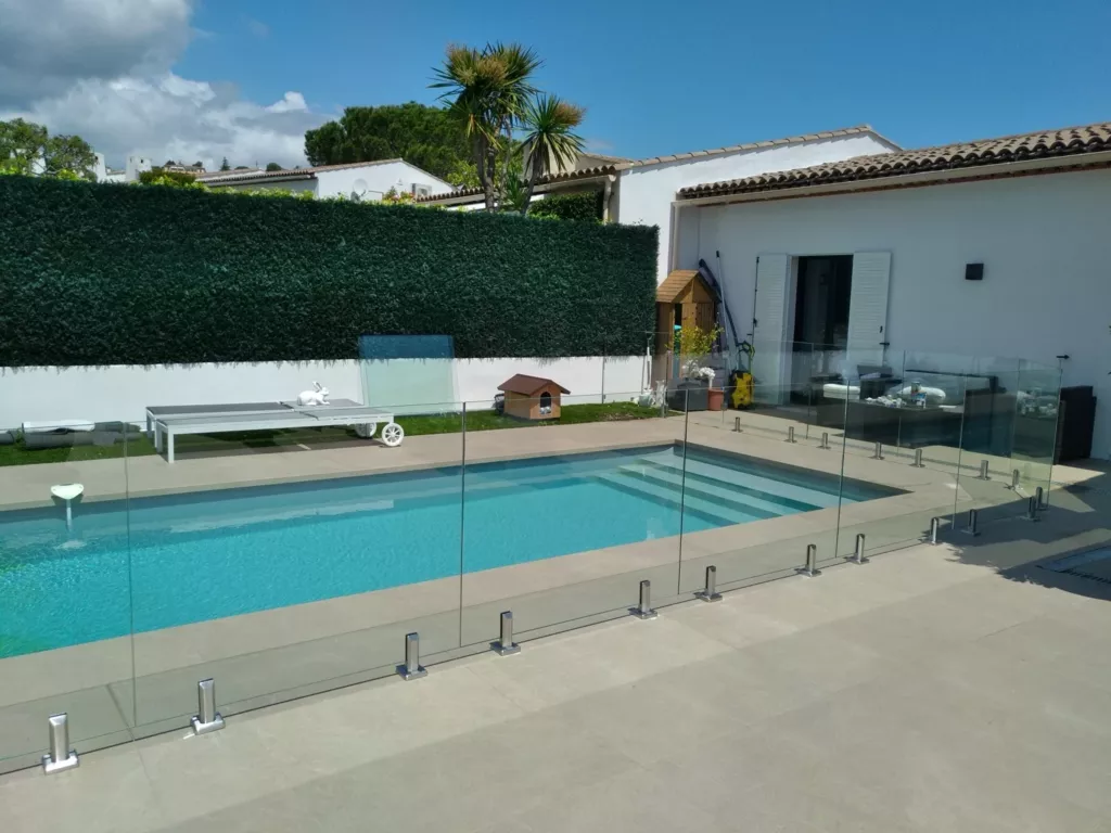 Clôture en panneaux de verre autour d’une piscine rectangulaire et de sa terrasse.