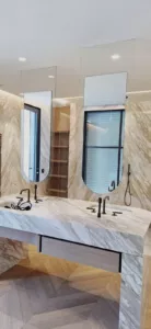 Deux grands miroirs aux contours arrondis au-dessus d’une double vasque en pierre veinée.