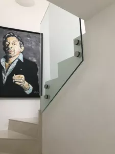 Panneau de garde-corps en verre suivant la pente d’un escalier, avec quatre fixations circulaires.