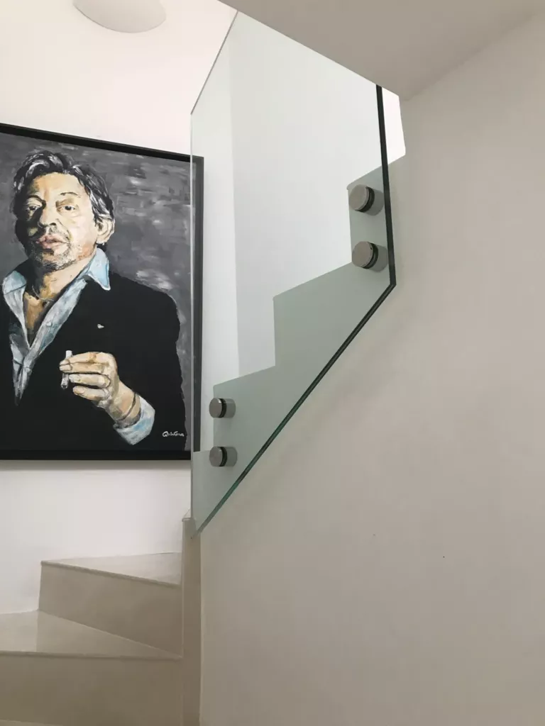 Panneau de garde-corps en verre suivant la pente d’un escalier, avec quatre fixations circulaires.