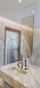 Miroir allongé aux angles inférieurs arrondis devant une salle de bains en pierre veinée.