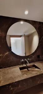 Grand miroir rond au-dessus d’une vasque et devant un mur en pierre sombre.