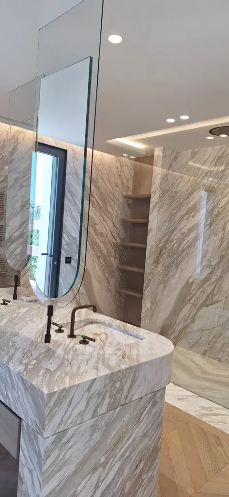 Miroirs allongés à base arrondie au-dessus d’un plan vasque, devant une douche vitrée.