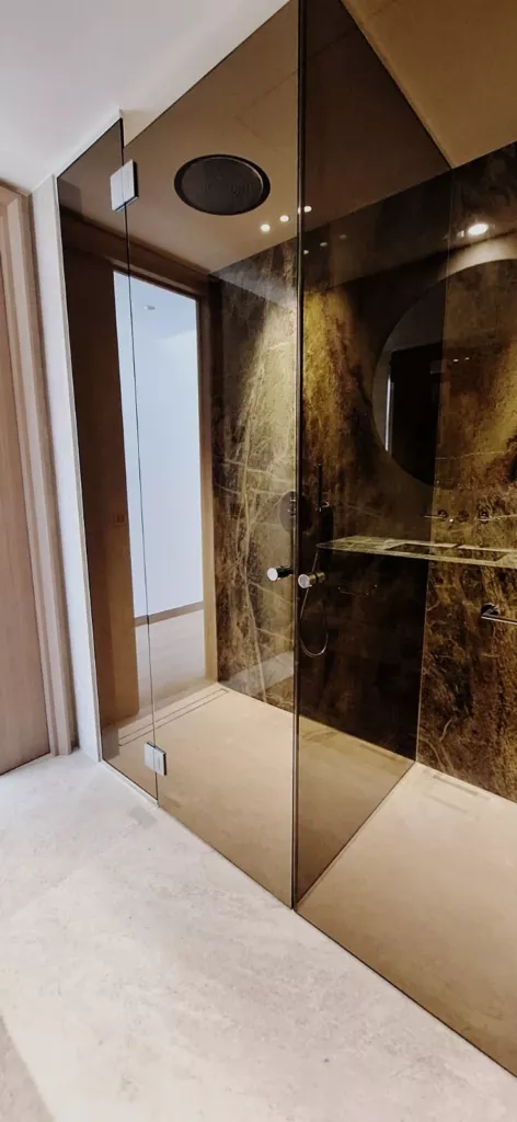 Porte vitrée et panneau fixe aux reflets bronze dans une douche habillée de pierre sombre.