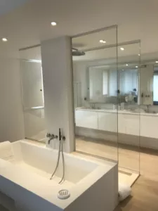 Salle de bains claire avec baignoire, grands miroirs et parois vitrées transparentes.