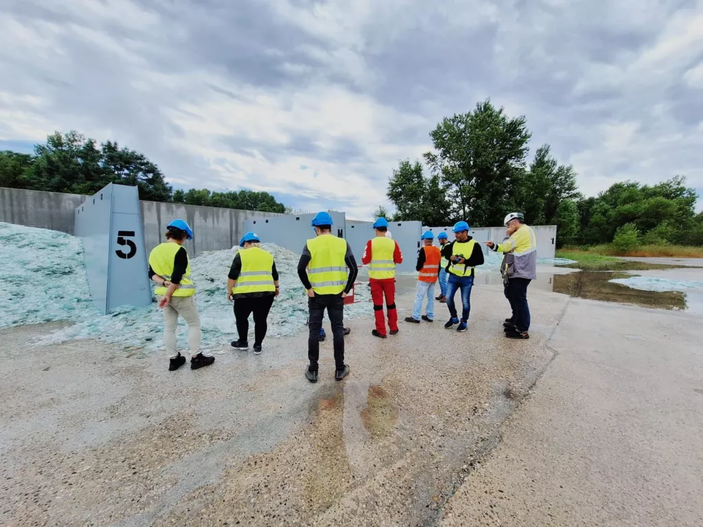 Groupe en visite, portant casques et gilets de signalisation, devant le stockage du verre sur le site Saint-Gobain de Salaise.